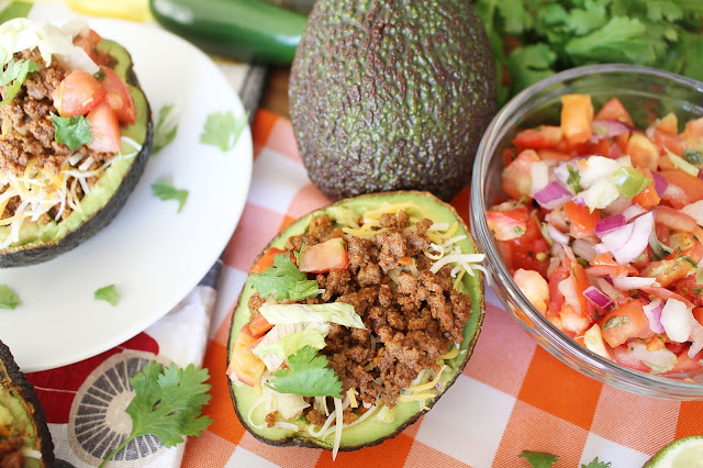 Halved avocado with beef, cheese, onion, tomato, cilantro and guacamole mixture - the Guano-Taco. Additional avocado and pico de Gallo ingredients in the background.
