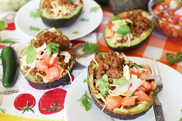 Halved avocado with beef, cheese, onion, tomato, cilantro and guacamole mixture - the Guano-Taco - on a plate with a fork, ready to eat.