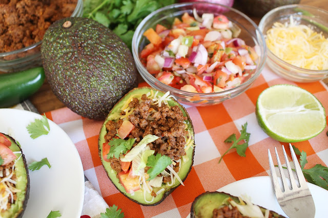 Halved avocado with beef, cheese, onion, tomato, cilantro and guacamole mixture - the Guano-Taco. Additional avocado, cheese, lime and pico de Gallo ingredients in the background.