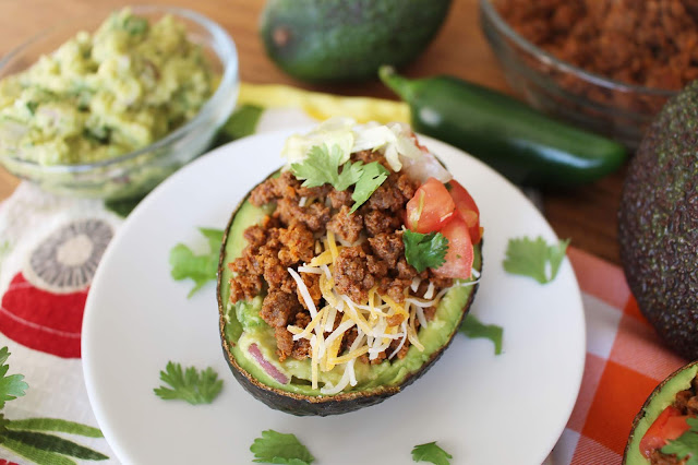 Halved avocado with beef, cheese, onion, tomato, cilantro and guacamole mixture - the Guano-Taco. Additional guacamole, jalapeño and ground beef ingredients in the background.