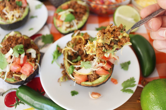 Halved avocados with beef, cheese, onion, tomato, cilantro and guacamole mixture - the Guano-Tacos. A fork bite of it is in the foreground about to be eaten.