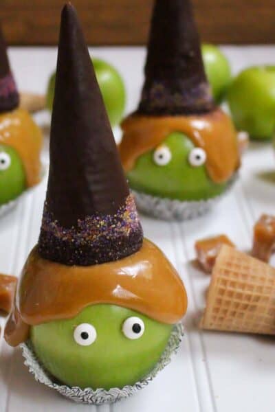 Multiple witch caramel apples topped with chocolate sugar cone witch hats and Halloween sprinkles sitting in cupcake liners