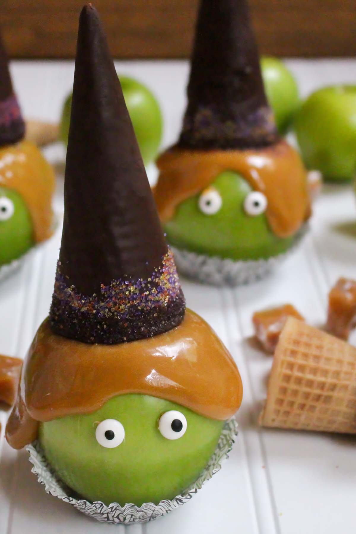 witch-caramel-apples-featured Multiple witch caramel apples topped with chocolate sugar cone witch hats and Halloween sprinkles sitting in cupcake liners