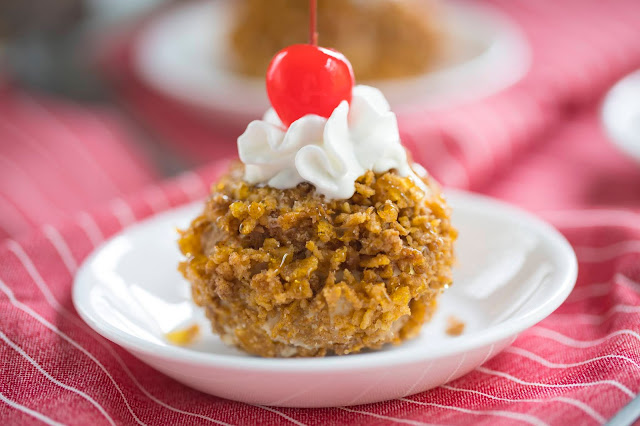 Easy "Fried" Ice Cream in a bowl with whipped cream and cherry on top. The fried ice cream is made of ice cream coated in crushed cereal.