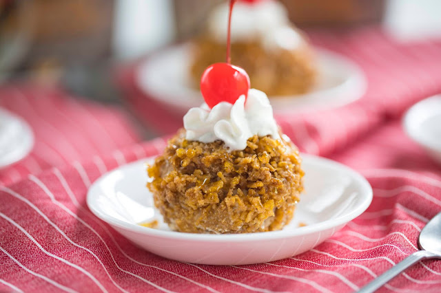 Easy "Fried" Ice Cream in a bowl with whipped cream and cherry on top. The fried ice cream is made of ice cream coated in crushed cereal.