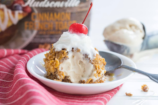 Easy "Fried" Ice Cream in a bowl with whipped cream and cherry on top. The fried ice cream is made of ice cream coated in crushed cereal. The fried ice cream has a bite taken out of it exposing the inside ice cream.