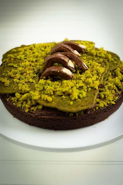 Zombie brownie cake topped with green cookies and a realistic Tootsie Roll zombie hand clawing out of the cake on a plate.