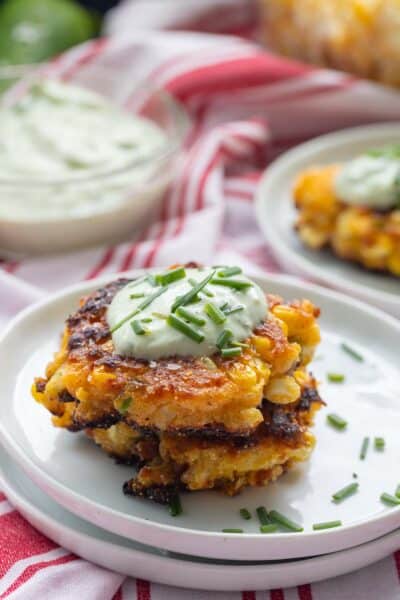 Close-up of spicy corn fritters topped with sour cream and chives on a white plate.
