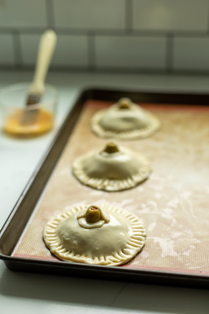 Uncooked savory Halloween Hand Pies shaped like eyeballs with a pimento olive center.