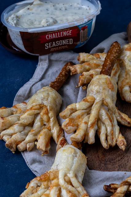 Savory witch broom made of puff pastry with a pretzel rod for the broomstick. Savory butter spread in the background.