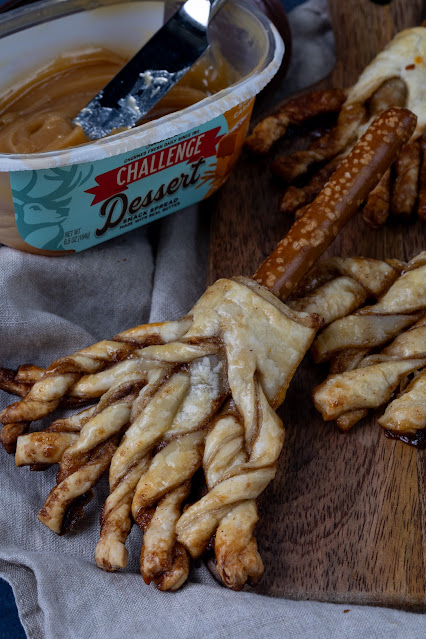 Sweet witch broom made of puff pastry with a pretzel rod for the broomstick. Dessert butter spread in the background.