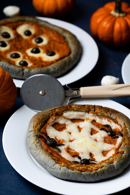 Halloween Pumpkin Pizzas with black crust and cheese/olive spider web design and cheese/olive eyeballs.