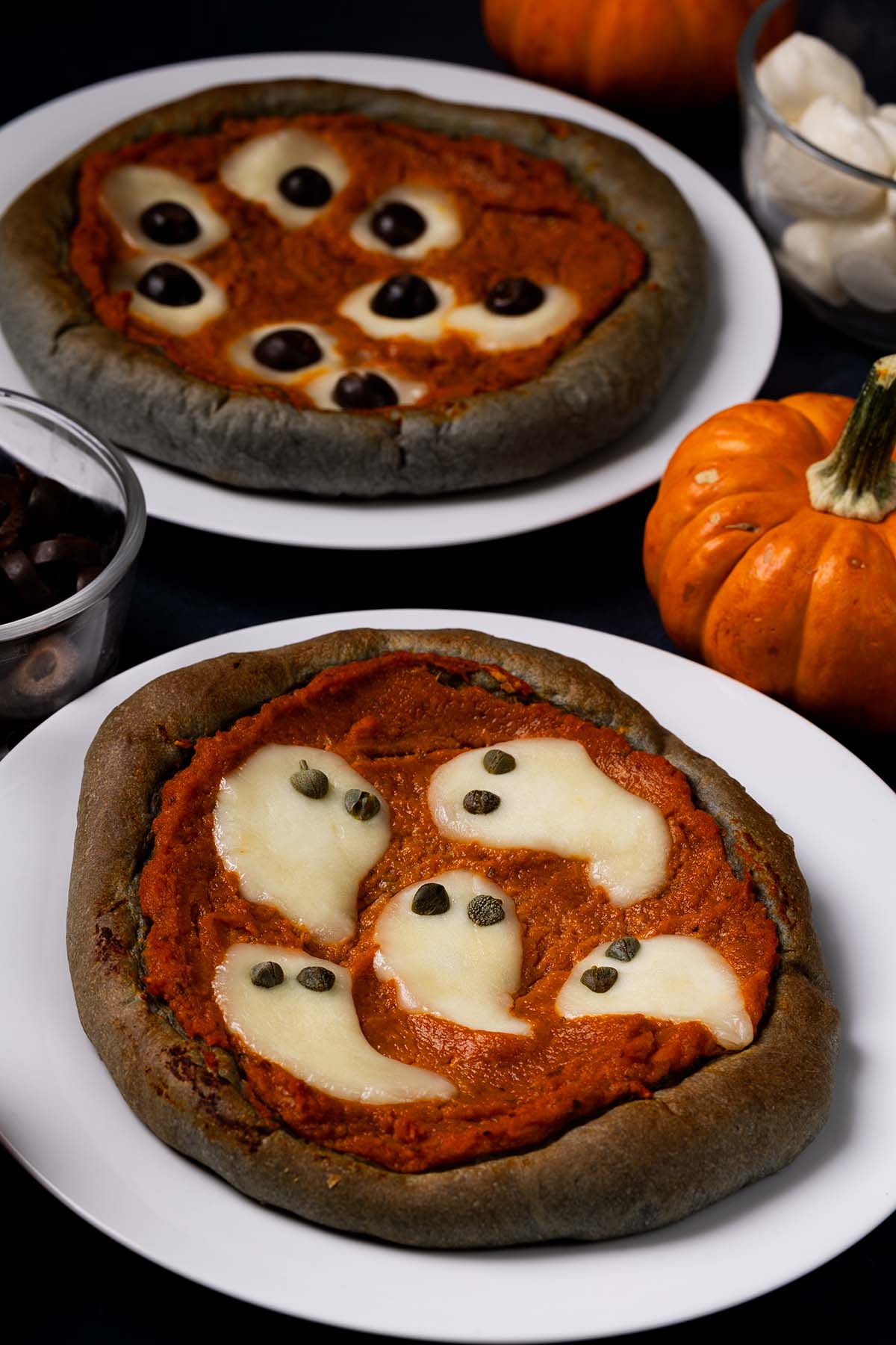 Halloween Pumpkin Pizzas with black crust and fun, spooky designs including cheese with caper ghosts and cheese and olive eye balls.