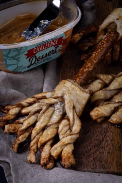 Sweet witch broom made of puff pastry with a pretzel rod for the broomstick. Dessert butter spread in the background.
