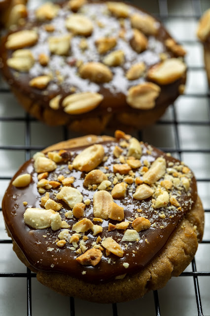 Tamarind Caramel Cookies on a baking sheet. The cookies are made of a brown sugar cookie with a tamarind caramel on top topped with sea salt and roasted peanuts. 