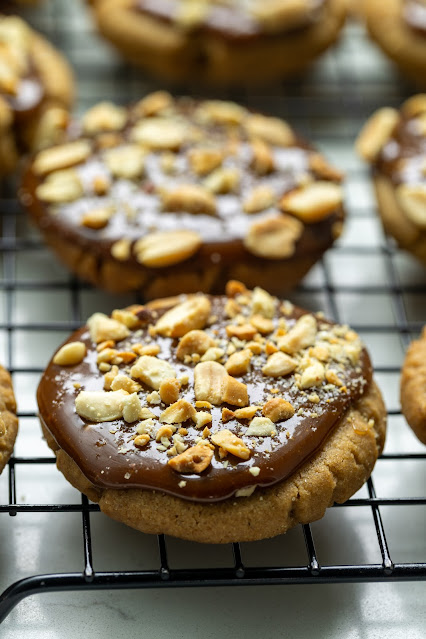 Tamarind Caramel Cookies on a baking sheet. The cookies are made of a brown sugar cookie with a tamarind caramel on top topped with sea salt and roasted peanuts. 