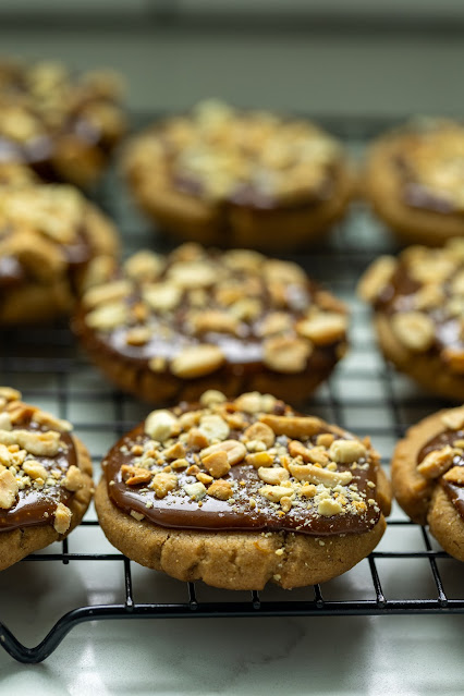 Tamarind Caramel Cookies on a baking sheet. The cookies are made of a brown sugar cookie with a tamarind caramel on top topped with sea salt and roasted peanuts. 