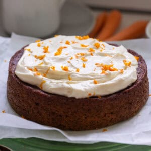 Completed carrot cake with carrot shavings on top, on a cake platter.