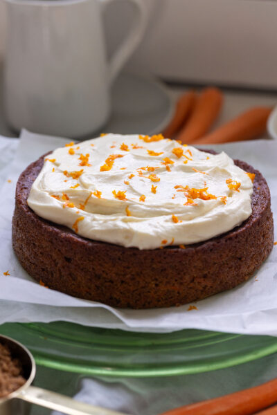 Completed carrot cake with carrot shavings on top, on a cake platter.