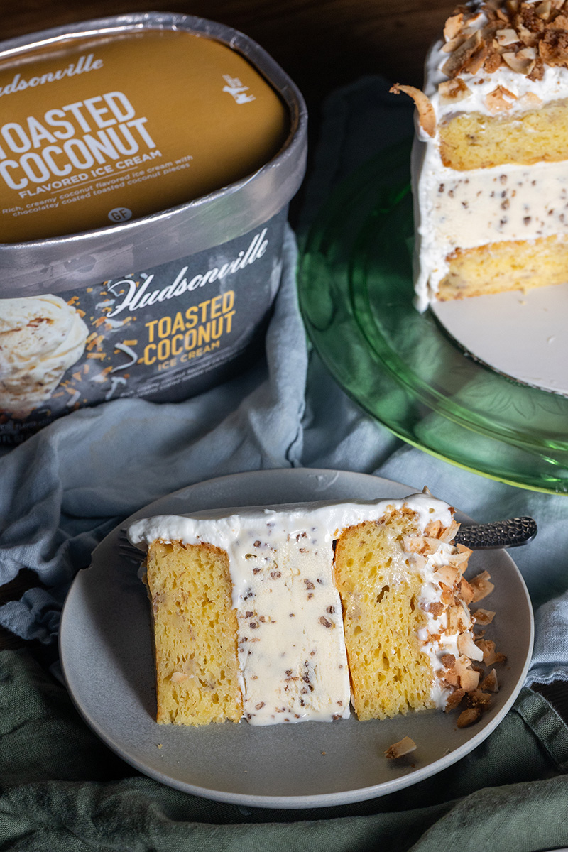 A side profile shot of a clean cut slice of homemade banana coconut ice cream cake showing precise layers of tender banana cake and premium coconut ice cream.