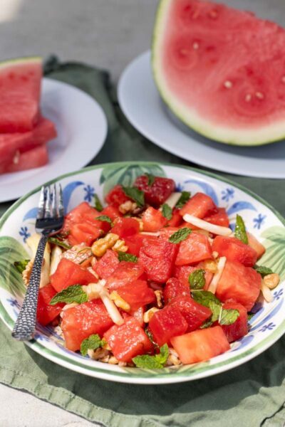 An individual portion of watermelon salad with matchstick fennel served in a blue and white bowl next to a fork.