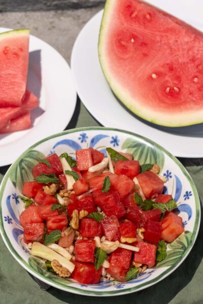 Overhead view of a bowl filled with cubed red watermelon, matchstick-cut fennel, toasted walnuts, and fresh mint.