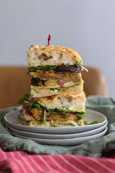 Stacked eggplant focaccia sandwiches with fresh greens on a white plate.