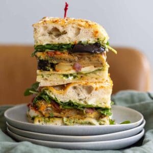Two make-ahead roasted eggplant focaccia sandwiches with pesto mayo stacked on top of each other on a kitchen table.