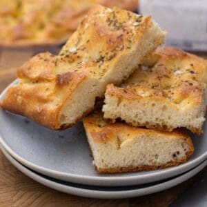 Easy homemade focaccia bread slices with a golden-brown blistered crust, and herby sea salt.