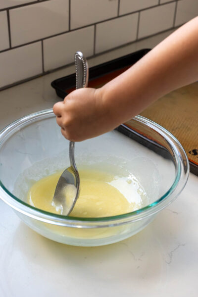 Little girl mixes melted butter in mixing bowl with spoon