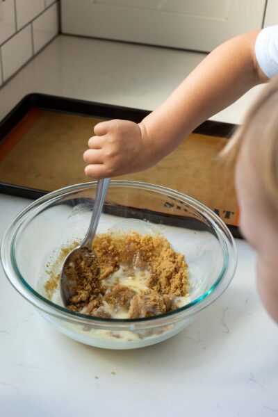 Little girl mixes brown sugar into mixing bowl with melted butter while little sister watches