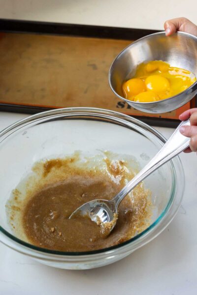 Little girl pours bowl of egg yolks into liquid ingredients for chocolate chip ice cream sandwich cookies