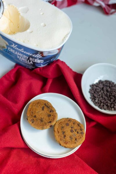 Two chocolate chip cookies on white plate ready to be filled with ice cream for ice cream sandwich cookies