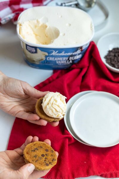 Vanilla ice cream on once chocolate chip cookie preparing to be sandwiched by second cookie