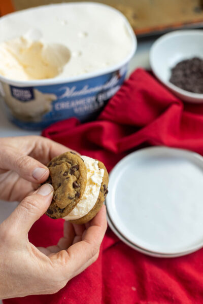 Hands press chocolate chip cookies into ice cream sandwich