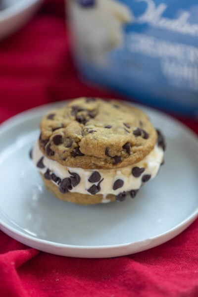 Close up shot of chocolate chip ice cream sandwich cookie on white plate with vanilla ice cream carton in background